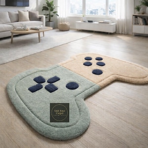 May include: A large, soft rug shaped like a video game controller. The rug is primarily light green and tan, with dark blue button details. The rug is on a hardwood floor in a living room setting.