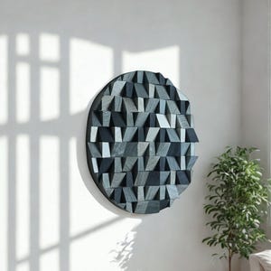 Könnte beinhalten: Runde, geometrische Wandkunst mit einem dunkelgrauen Rahmen. Das Kunstwerk hat eine strukturierte Oberfläche aus kleinen, abgewinkelten Holzblöcken in Grau- und Blautönen. Es ist an einer weißen Wand montiert, mit Schatten von einem Fenster.
