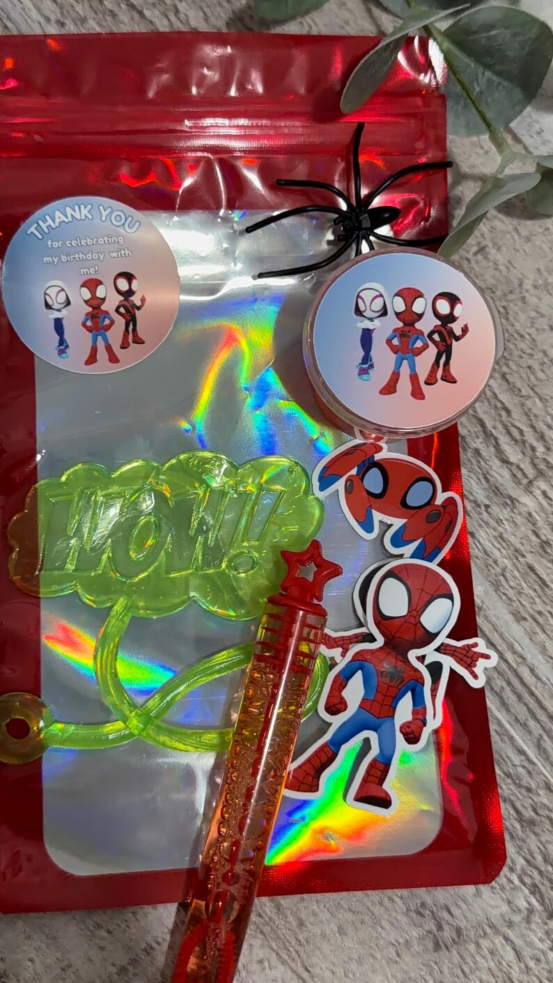 May include: A red cellophane bag with a holographic interior, featuring Spider-Man themed party favors. Includes stickers, a bubble wand, and a green "WOW!" speech bubble. The bag has a black spider decoration.