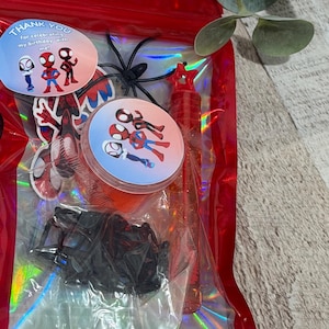 May include: A red cellophane bag filled with Spider-Man themed party favors. Includes stickers, a bubble wand, and plastic spiders. The stickers have the text "Thank you for celebrating my birthday with me!"