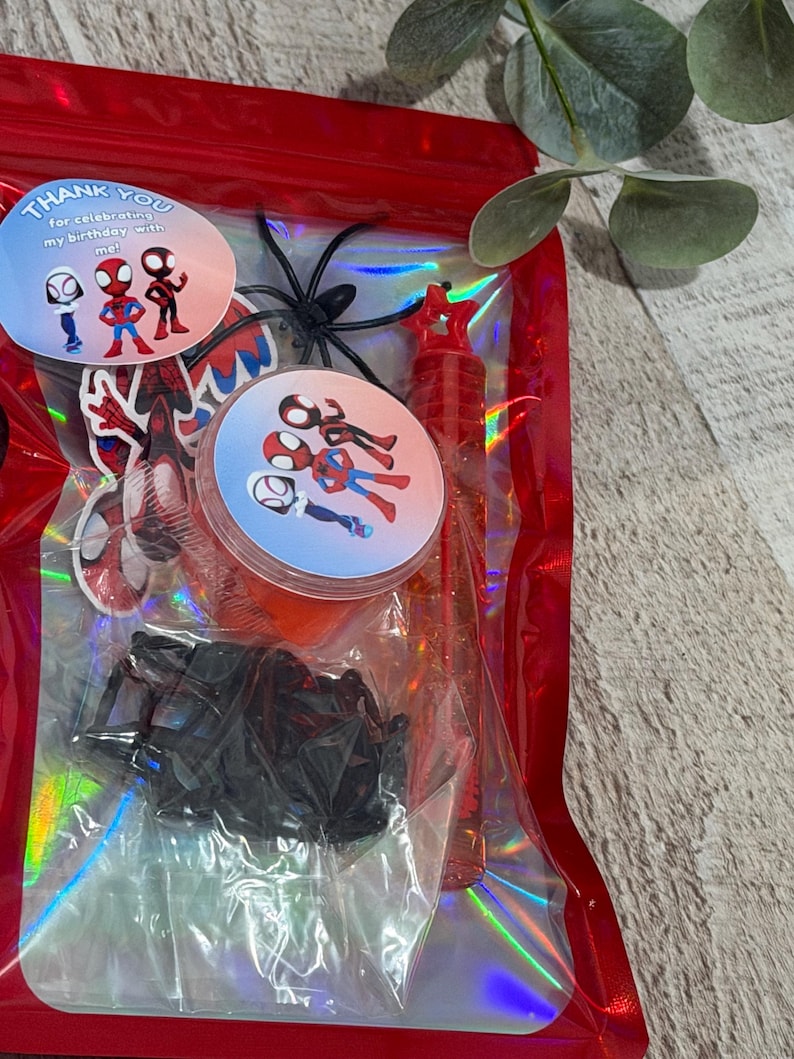 May include: A red cellophane bag filled with Spider-Man themed party favors. Includes stickers, a bubble wand, and plastic spiders. The stickers have the text "Thank you for celebrating my birthday with me!"