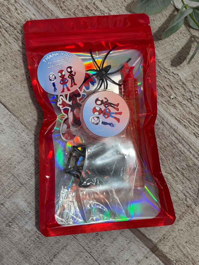 May include: A red cellophane bag filled with Spider-Man themed party favors. The bag contains stickers, a pen, a plastic spider, and two circular stickers that read "Thank you for celebrating my birthday with me!"