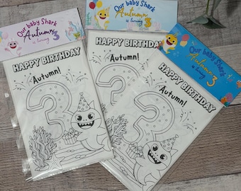 May include: Three coloring pages in plastic sleeves with a Baby Shark theme. Each page says "Happy Birthday Autumn!" and features a large number 3 with a shark wearing a party hat. The top banner reads "Our baby Shark Autumn is turning 3".