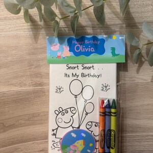 Peut inclure: Un ensemble de coloriage sur le th&egrave;me de l'anniversaire avec des personnages de Peppa Pig. L'ensemble comprend un livre de coloriage avec le texte "Snort Snort... It's My Birthday!!" et "Happy Birthday Olivia", des crayons et un autocollant rond. Les crayons sont orange, bleu et vert.