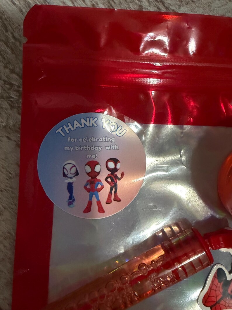 May include: A red plastic bag with a clear window, containing a bubble wand and a round sticker. The sticker says "Thank You for celebrating my birthday with me!" and features three cartoon Spider-Man characters.