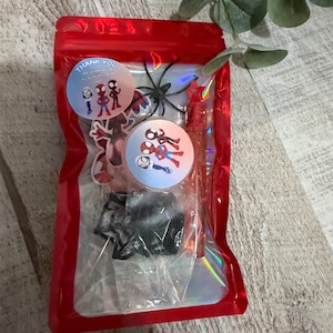 May include: A red cellophane bag filled with party favors. Inside are stickers with Spider-Man characters, a black plastic spider, and a red candy stick. The bag has a holographic sheen and the text "Thank You".