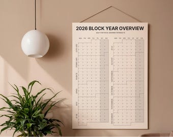Puede incluir: Se muestra un calendario de resumen del año 2026, con una paleta de colores neutros. El calendario está suspendido de una pared, con una lámpara colgante esférica blanca y una planta en maceta en primer plano. El calendario está diseñado para el enfoque y los resultados.