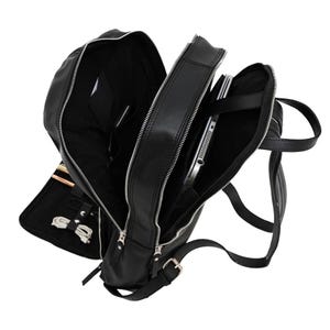 May include: A black backpack with multiple zipped compartments, featuring silver-toned hardware. The interior reveals a dedicated laptop sleeve, internal pockets, and elastic loops for organising small items like cables and pens.