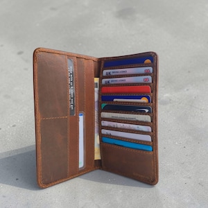 May include: Open brown leather wallet with multiple card slots filled with cards and cash. The wallet is rectangular and has a textured appearance. The interior is lined with a lighter brown material. The wallet is open, displaying its contents.
