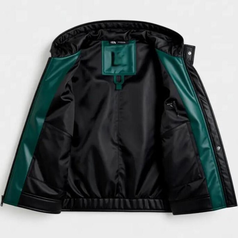 May include: Black jacket with a hood and green trim. The interior is black with a green patch featuring the letter "L". The jacket has two pockets and a zipper closure. The jacket is made of a smooth, possibly leather-like material.