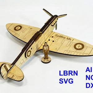 May include: A wooden model of a Spitfire Mk I airplane with a pilot figurine. The model is light brown with dark brown detailing, including the propeller and markings. The text "Spitfire Mk I" is visible on the wing. The model is accompanied by the text "LBRN SVG AI NC DXF".