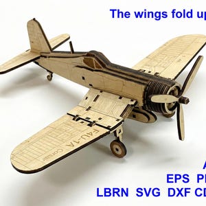 Puede incluir: Un modelo de avión de madera cortado con láser con el texto F4U-1A Corsair en el ala. El modelo incluye una hélice, tren de aterrizaje y alas que se pliegan. El texto The wings fold up! aparece arriba, con AI, EPS, PDF, LBRN, SVG, DXF, CDR.