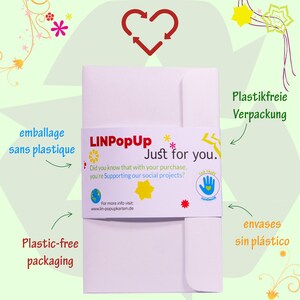 May include: A white envelope with a pink band that says "LINPopUp Just for you." The band also includes a small globe, a yellow star, and a red star. The text "Did you know that with your purchase, you're supporting our social projects?" is printed on the band. The envelope is labeled "Plastic-free packaging" and "Plastikfreie Verpackung".