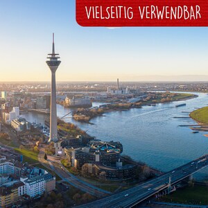 May include: An aerial view of a city with a tall, slender tower in the foreground. The tower is white and has a red tip. The city is surrounded by water and there is a bridge in the distance.