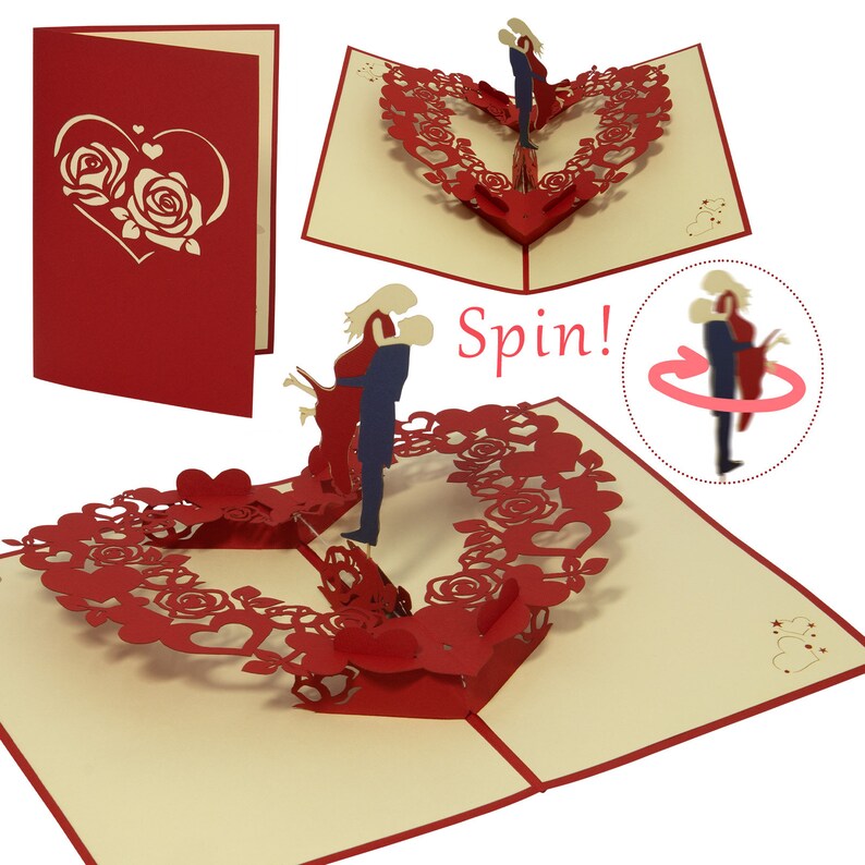 May include: A red and cream pop-up card featuring a couple kissing within a heart-shaped wreath of roses. The card is open, showcasing the couple. The text "Spin!" is printed on the card.
