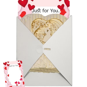 Peut inclure: Une enveloppe blanche contenant une carte pop-up. La carte est en forme de c&oelig;ur et pr&eacute;sente un design 3D d'un couple dans un cadre romantique. L'enveloppe a un motif de c&oelig;ur rouge sur le devant et le texte "Just for You." au dos.