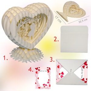 Peut inclure: Une carte pop-up 3D blanche en forme de c&oelig;ur avec un couple &agrave; l'int&eacute;rieur. La carte mesure 17 cm de large et 20,5 cm de haut. La carte est livr&eacute;e avec une enveloppe blanche et une carte rose avec le texte "Just for You."