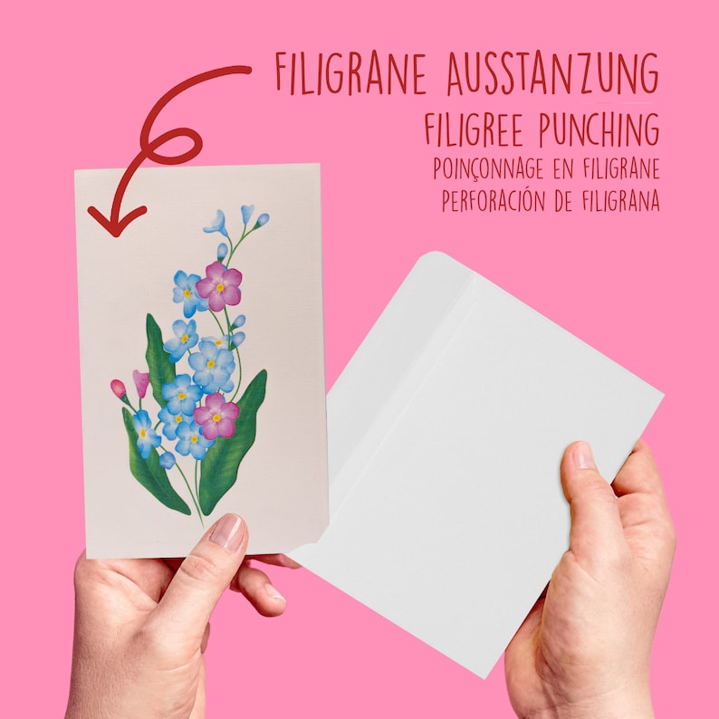 May include: A white card with a painted image of blue and pink flowers. The card is being held by a hand and is being placed into a white envelope. The text "FILIGRANE AUSSTANZUNG FILIGREE PUNCHING POIN&Ccedil;ONNAGE EN FILIGRANE PERFORACI&Oacute;N DE FILIGRANA" is printed on the envelope.