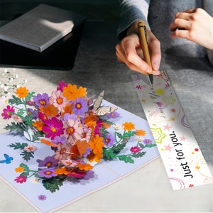 Peut inclure: Une carte 3D pop-up avec un bouquet de fleurs color&eacute;es et des papillons. La carte porte un message qui dit "Just for you. I wish you..."
