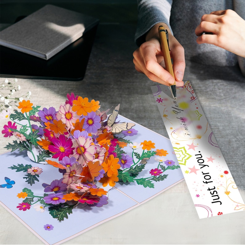 Peut inclure: Une carte 3D pop-up avec un bouquet de fleurs color&eacute;es et des papillons. La carte porte un message qui dit "Just for you. I wish you..."