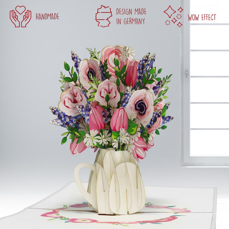 May include: A handmade pop-up card featuring a bouquet of pink and white flowers, including tulips and anemones, in a cream-colored vase. The card has the text "DESIGN MADE IN GERMANY" and "WOW EFFECT".