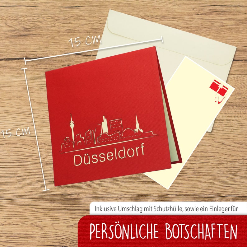 May include: Red 3D pop-up card featuring a cityscape of D&uuml;sseldorf, Germany. The card is 15 cm wide and 15 cm tall. It includes a white envelope with a red gift box icon.