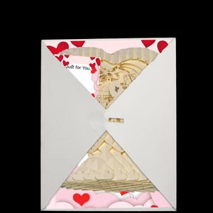 Peut inclure: Une enveloppe blanche contenant une carte en forme de c&oelig;ur rose et blanche. La carte pr&eacute;sente un design en papier d&eacute;coup&eacute; en 3D d'un c&oelig;ur avec un nichoir &agrave; oiseaux et des fleurs. La carte porte le texte "Just for You." imprim&eacute; dessus.