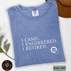 May include: A blue jean colored short-sleeve t-shirt with a crew neckline. The front features white text that reads I CAME. I ENGINEERED. I RETIRED. accompanied by a circular icon with a hand pressing a button labeled END.