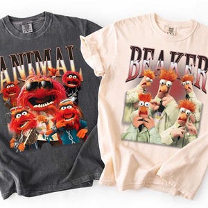 Puede incluir: Dos camisetas gráficas. Una es de color gris carbón con la palabra "ANIMAL" encima de un gráfico del personaje de los Muppets Animal. La otra es de color beige claro con la palabra "BEAKER" encima de un gráfico del personaje de los Muppets Beaker.