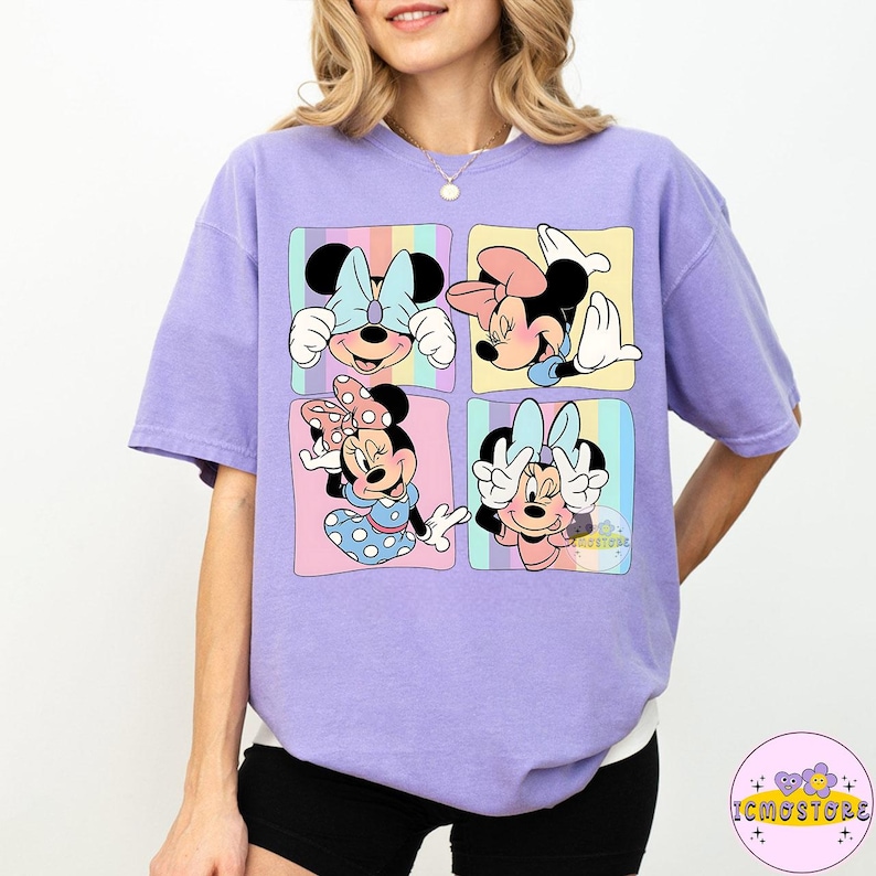May include: A light purple t-shirt featuring a colorful graphic of Minnie Mouse in four different poses. Each pose is set within a pastel-colored square. The shirt has short sleeves and a relaxed fit.