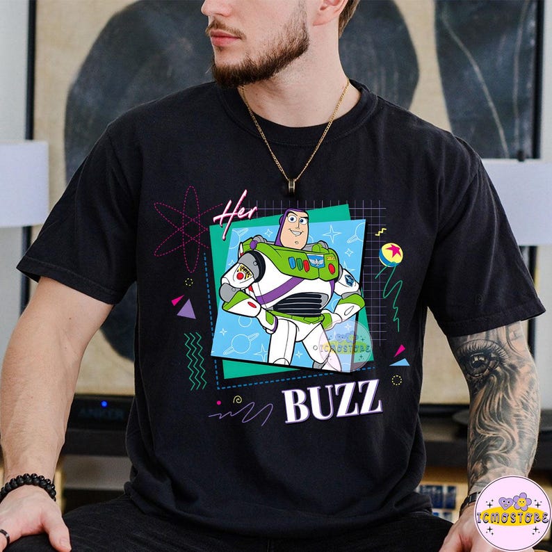 May include: Black t-shirt featuring a graphic of Buzz Lightyear from Toy Story. The design includes the word "BUZZ" and the word "Her" with a retro 90s style design. The character is in a square frame with a blue background.