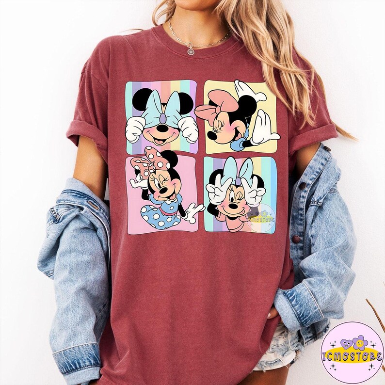 May include: A maroon t-shirt featuring a colorful graphic of Minnie Mouse in four different poses. Each pose is set within a square with a pastel rainbow background. The shirt has short sleeves and a relaxed fit.
