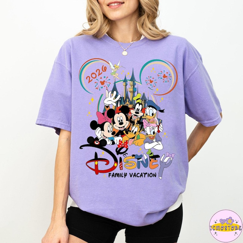 May include: A light purple t-shirt featuring a colorful graphic of Disney characters, including Mickey and Minnie Mouse, Goofy, Donald Duck, and Daisy Duck. The text "Disney Family Vacation 2026" is also displayed.