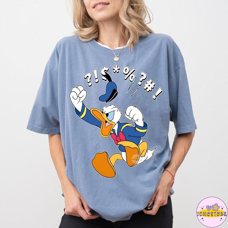 May include: A light blue t-shirt featuring a cartoon image of Donald Duck in a fit of anger, with symbols above his head. Donald Duck is wearing a blue sailor suit and a red bow tie. The shirt is a comfortable, oversized fit.