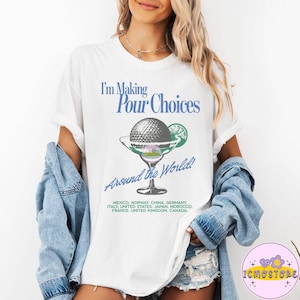 May include: A white short-sleeve t-shirt featuring a graphic of a cocktail glass with a lime wedge and the text I'm Making Pour Choices Around the World! followed by a list of countries including Mexico, Norway, China, Germany, Italy, United States, Japan, Morocco, France, United Kingdom, and Canada.