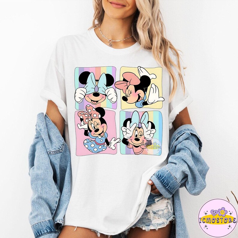 May include: White t-shirt featuring a colorful graphic of Minnie Mouse in four different poses. Each pose is set within a pastel-colored square. The design includes Minnie's iconic bow and polka dots. The shirt is part of the Disney collection.