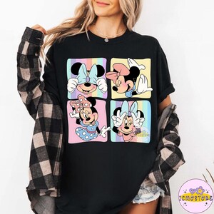 May include: Black t-shirt featuring a colorful graphic of Minnie Mouse in four different poses. Each pose is set within a pastel-colored square. The shirt has a crew neck and short sleeves. The text "ICMOSTORE" is visible on the bottom right.