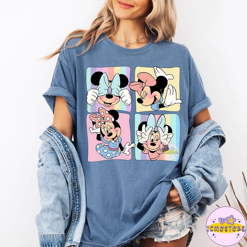 May include: Blue t-shirt featuring four panels with Minnie Mouse illustrations. Each panel has a different pose and background color, including pink, yellow, and blue. Minnie Mouse is wearing a bow in each panel.