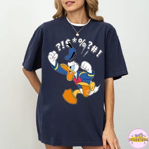 May include: Navy blue t-shirt featuring a cartoon image of Donald Duck in a fit of anger, with speech bubbles containing symbols. The character is wearing his signature sailor suit and hat. The shirt is a comfortable, oversized fit.