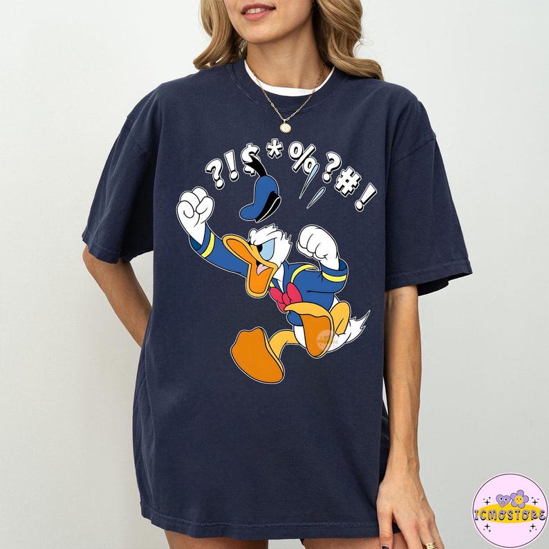 May include: Navy blue t-shirt featuring a cartoon image of Donald Duck in a fit of anger, with speech bubbles containing symbols. The character is wearing his signature sailor suit and hat. The shirt is a comfortable, oversized fit.