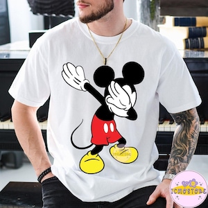 Puede incluir: Camiseta blanca con una ilustraci&oacute;n de dibujos animados de Mickey Mouse haciendo un dab. Mickey lleva pantalones cortos rojos, zapatos amarillos y guantes negros. La camiseta tiene el texto "ICMOSTORE" en el zapato.