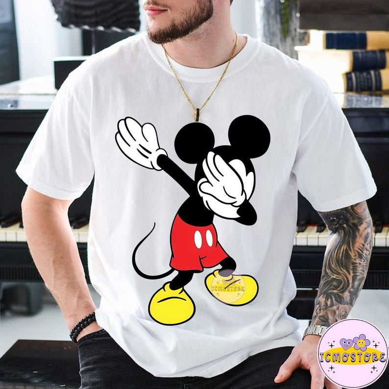 Puede incluir: Camiseta blanca con una ilustraci&oacute;n de dibujos animados de Mickey Mouse haciendo un dab. Mickey lleva pantalones cortos rojos, zapatos amarillos y guantes negros. La camiseta tiene el texto "ICMOSTORE" en el zapato.