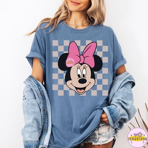 Puede incluir: Camiseta azul con un dise&ntilde;o de Minnie Mouse, un lazo rosa y un fondo a cuadros. El dise&ntilde;o incluye el texto "Wonderful". Forma parte de una colecci&oacute;n de ropa.