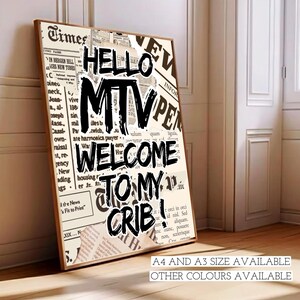 May include: Framed wall art featuring a collage of newspaper cuttings. The artwork displays the text "HELLO MTV WELCOME TO MY CRIB!" in bold black lettering. The print is in a wooden frame, set against a neutral wall and wooden floor.