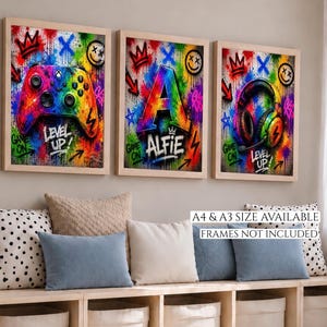 May include: Three framed art prints with a gaming theme. The prints feature a colourful controller, the letter "A" with the name "Alfie", and headphones. Each print has graffiti-style elements and the words "Level Up" and "Game On".