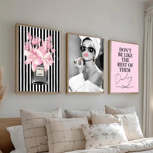 May include: A set of three framed prints. One shows pink flowers in a perfume bottle against black and white stripes. Another depicts a woman applying lipstick. The third has the text "Don't be like the rest of them Darling."