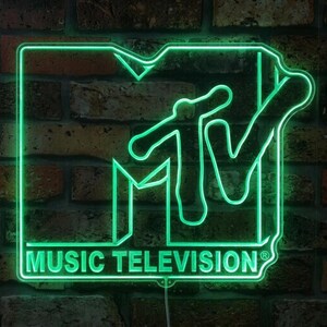 May include: A bright green neon sign displaying the MTV logo with the text MUSIC TELEVISION underneath. The sign features a bold, outlined block letter M and a stylized V, emitting a vibrant glow that illuminates the surrounding area.