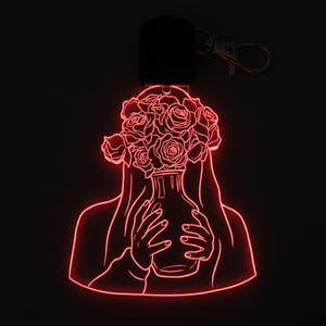 May include: A red LED keyring depicting a woman holding a vase of roses. The outline of the woman and roses is illuminated against a black backdrop. The keyring has a black top and a silver clasp.