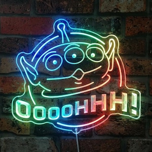 May include: A neon sign featuring a three-eyed alien character with pointed ears and a rounded head. The light glows in a gradient of blue, green, and orange. Below the character, the text OOOOHHH! is illuminated in the same neon style.