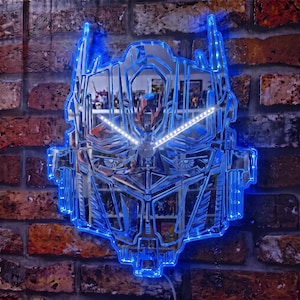 Peut inclure: Une horloge murale en forme de tête robotique avec une surface miroir réfléchissante et un éclairage LED bleu vif soulignant les détails mécaniques complexes. L'horloge présente deux aiguilles blanches lumineuses centrées sur le design.